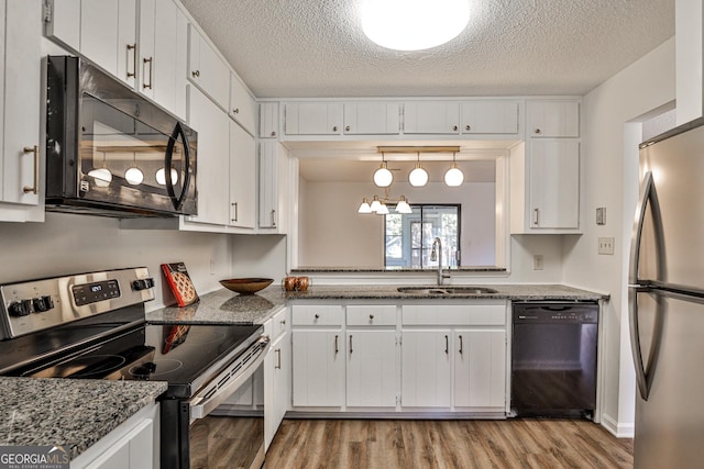 kitchen featuring light wood-style floors, black appliances, white cabinetry, pendant lighting, and a sink