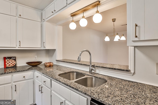 kitchen featuring hanging light fixtures, dark stone countertops, a sink, and white cabinetry