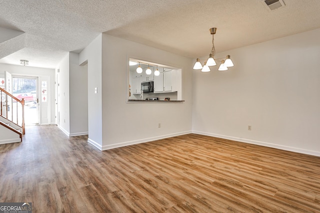 interior space with a notable chandelier, wood finished floors, visible vents, baseboards, and stairway