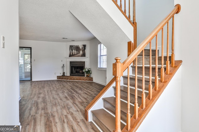 stairway with a brick fireplace, a textured ceiling, baseboards, and wood finished floors