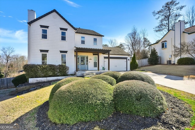 traditional-style house featuring a garage, a chimney, fence, and concrete driveway