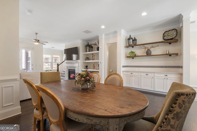 dining room featuring a warm lit fireplace, dark wood-style floors, crown molding, and recessed lighting