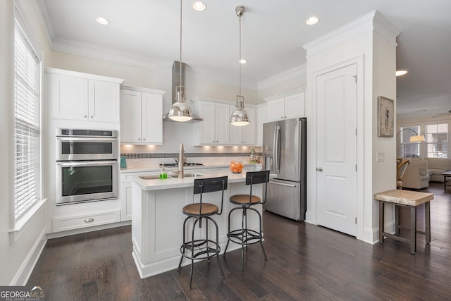 kitchen featuring decorative light fixtures, light countertops, appliances with stainless steel finishes, a kitchen island with sink, and white cabinets