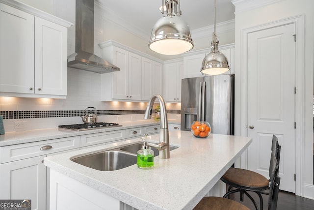 kitchen featuring white cabinetry, ornamental molding, wall chimney range hood, appliances with stainless steel finishes, and decorative light fixtures