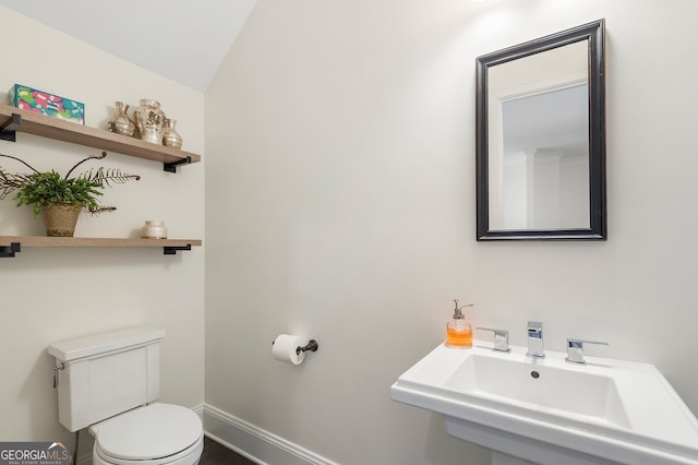 half bathroom with toilet, baseboards, and a sink