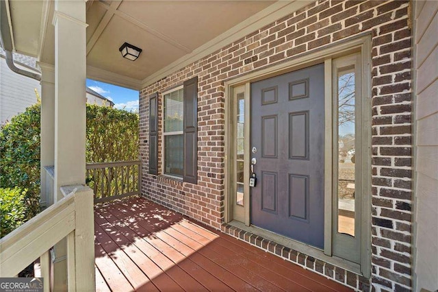 doorway to property featuring covered porch and brick siding