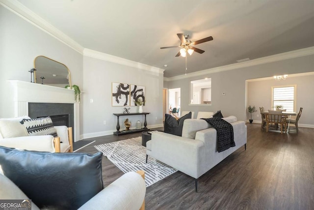 living room featuring dark wood-style flooring, a fireplace, ornamental molding, baseboards, and ceiling fan with notable chandelier