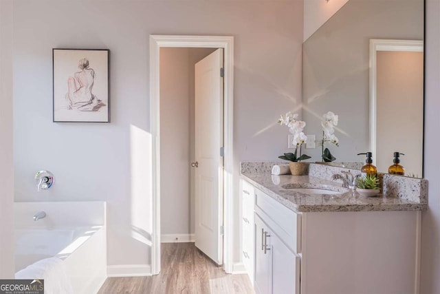 full bath with baseboards, vanity, a bath, and wood finished floors