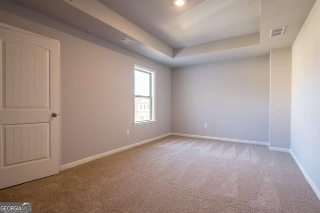 carpeted spare room featuring a raised ceiling, visible vents, and baseboards