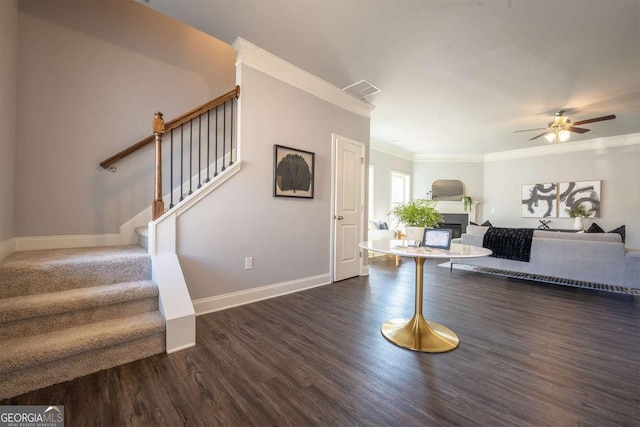 interior space with crown molding, dark wood-type flooring, a glass covered fireplace, baseboards, and stairs