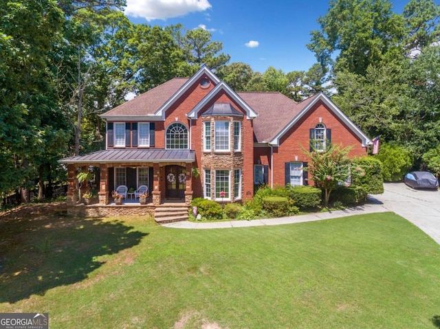 view of front of property with metal roof, covered porch, a standing seam roof, a front yard, and brick siding