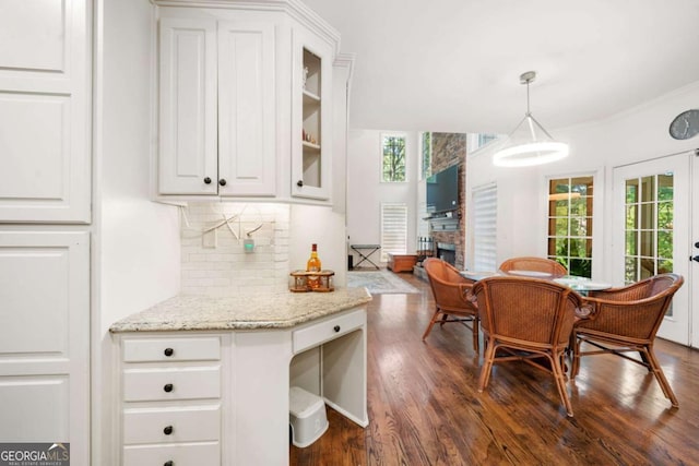 kitchen with a fireplace, white cabinets, hanging light fixtures, tasteful backsplash, and glass insert cabinets