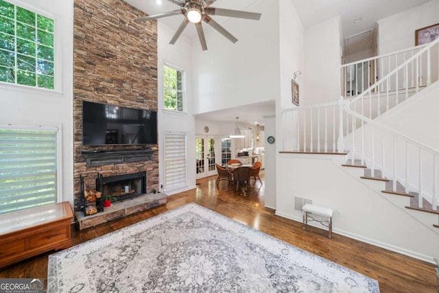 living area with stairway, a high ceiling, a stone fireplace, wood finished floors, and baseboards