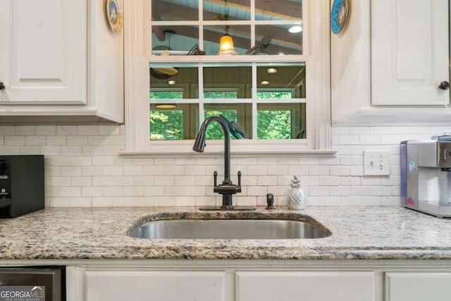 kitchen featuring decorative backsplash, light stone counters, white cabinets, and a sink