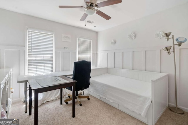 home office with visible vents, a decorative wall, a ceiling fan, wainscoting, and light carpet