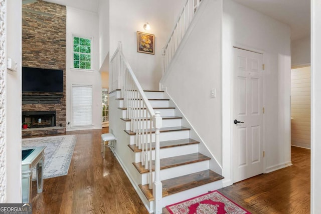 stairs with a stone fireplace, wood finished floors, and a towering ceiling