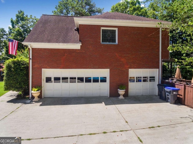 view of side of home with an attached garage, driveway, roof with shingles, and brick siding