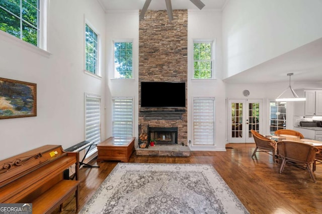 living room featuring dark wood-type flooring, a high ceiling, a fireplace, french doors, and crown molding