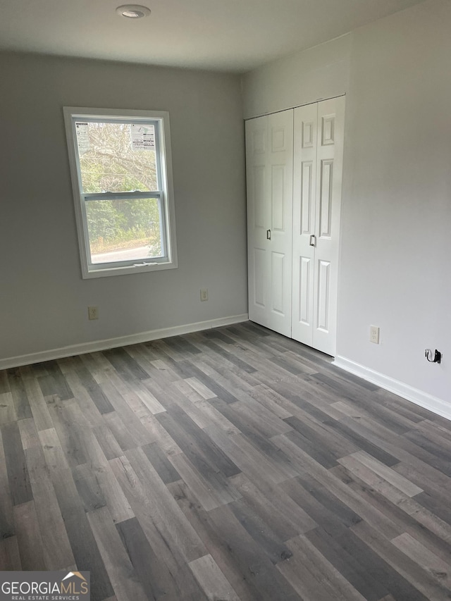 unfurnished bedroom featuring a closet, dark wood-style flooring, and baseboards