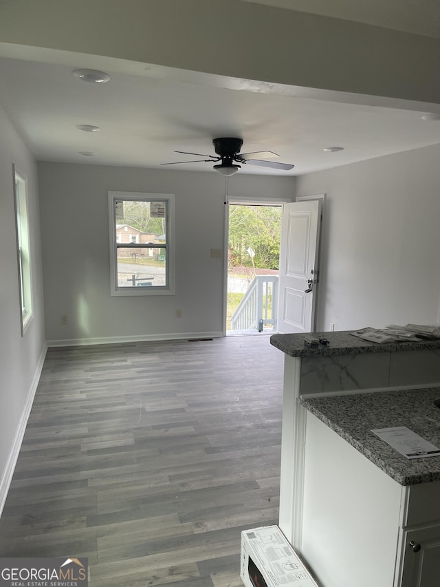 unfurnished living room featuring a healthy amount of sunlight, a ceiling fan, baseboards, and wood finished floors