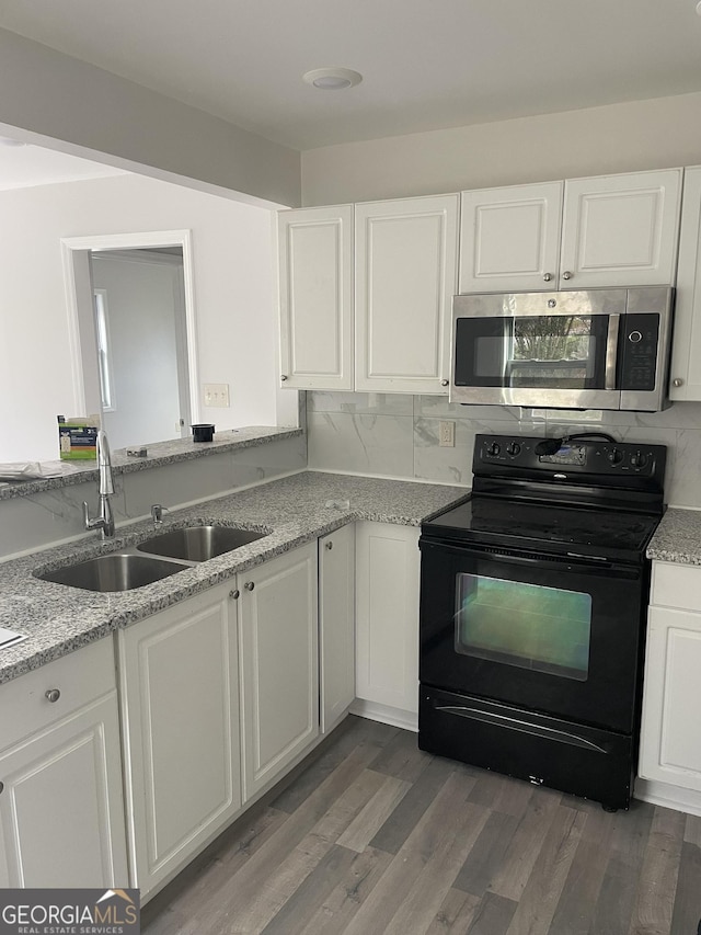 kitchen featuring black electric range, stainless steel microwave, a sink, and white cabinets