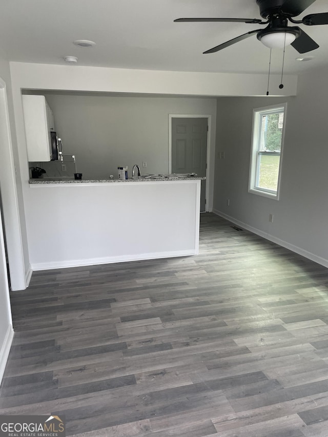 unfurnished living room with dark wood-style flooring, a sink, a ceiling fan, and baseboards