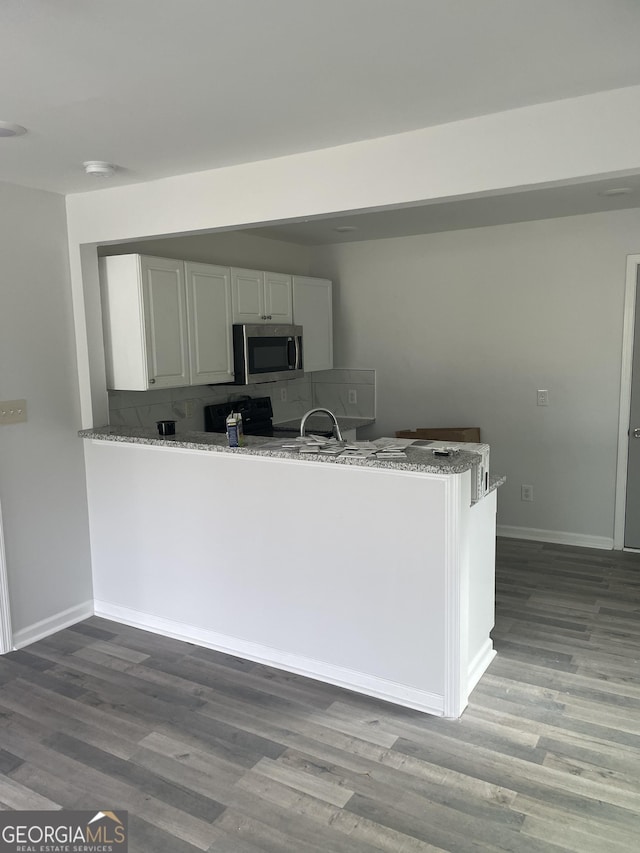 kitchen featuring stainless steel microwave, a peninsula, light stone countertops, white cabinetry, and backsplash