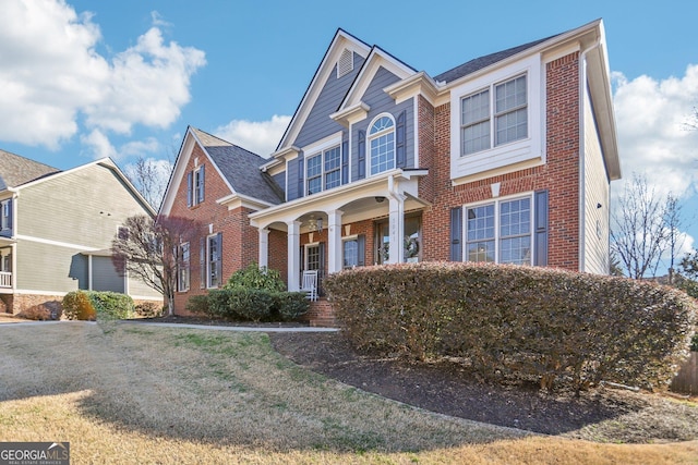 view of front of home with covered porch, brick siding, and a front lawn