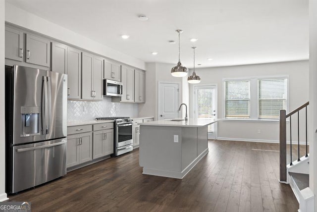 kitchen featuring stainless steel appliances, gray cabinets, light countertops, and a center island with sink