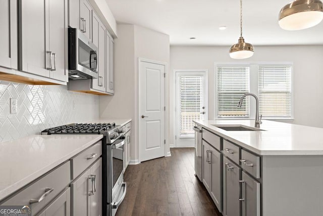 kitchen with pendant lighting, stainless steel appliances, gray cabinets, light countertops, and a sink