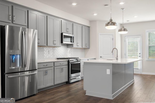 kitchen featuring stainless steel appliances, gray cabinetry, light countertops, and an island with sink