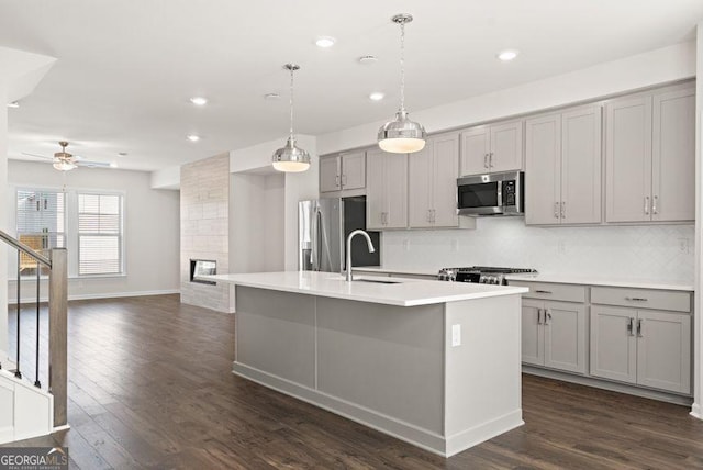 kitchen featuring an island with sink, hanging light fixtures, stainless steel appliances, light countertops, and gray cabinetry