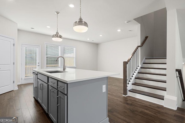 kitchen featuring decorative light fixtures, a center island with sink, gray cabinets, light countertops, and a sink