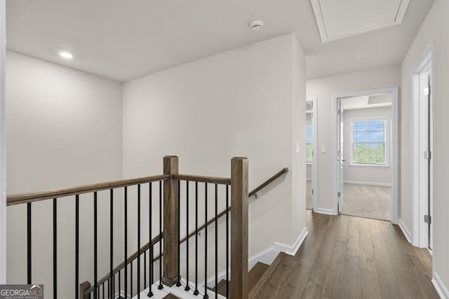 corridor featuring attic access, baseboards, dark wood-type flooring, and an upstairs landing