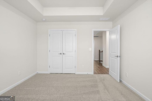 unfurnished bedroom with carpet floors, a tray ceiling, a closet, and baseboards