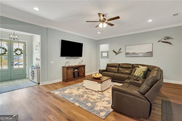 living room with baseboards, visible vents, wood finished floors, crown molding, and ceiling fan with notable chandelier