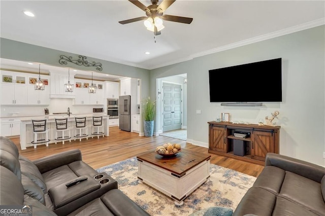 living area with light wood finished floors, ceiling fan, ornamental molding, and baseboards