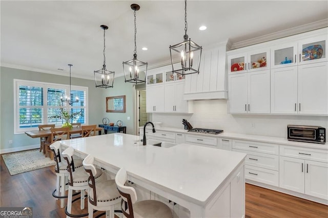 kitchen with a sink, a center island with sink, glass insert cabinets, and pendant lighting