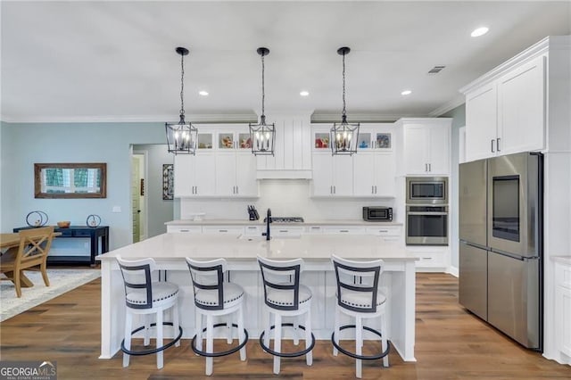 kitchen with glass insert cabinets, a center island with sink, appliances with stainless steel finishes, and light countertops