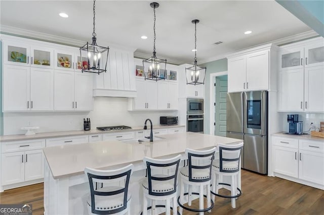 kitchen with stainless steel appliances, light countertops, glass insert cabinets, white cabinets, and a kitchen island with sink