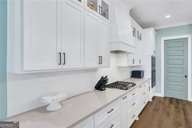 kitchen featuring tasteful backsplash, white cabinets, glass insert cabinets, ornamental molding, and premium range hood