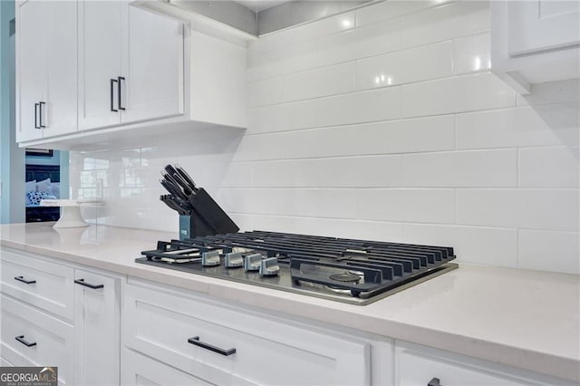 kitchen featuring stainless steel gas cooktop, white cabinetry, light countertops, and decorative backsplash