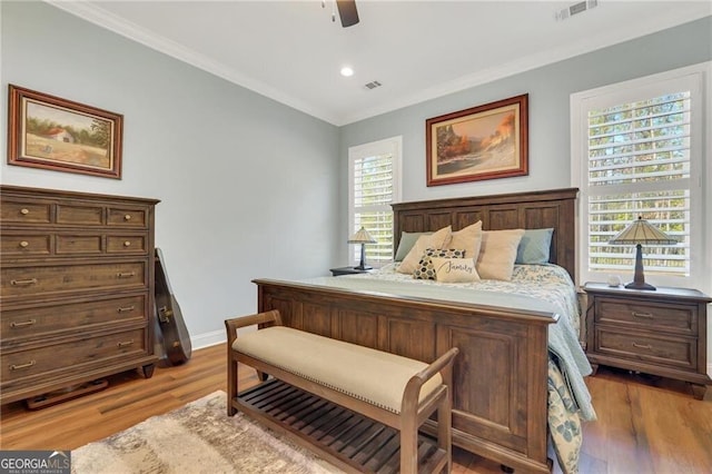 bedroom with baseboards, wood finished floors, visible vents, and crown molding