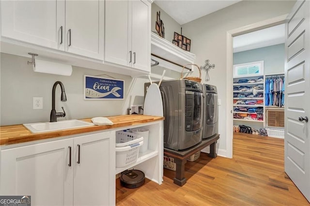 laundry room featuring light wood-type flooring, cabinet space, a sink, and washing machine and clothes dryer