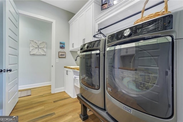 washroom featuring light wood finished floors, independent washer and dryer, cabinet space, and baseboards