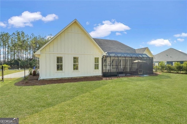 rear view of house featuring a lanai, board and batten siding, fence, and a lawn