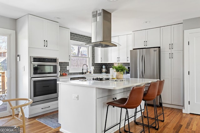 kitchen featuring stainless steel appliances, a kitchen island, white cabinetry, light wood-type flooring, and island exhaust hood