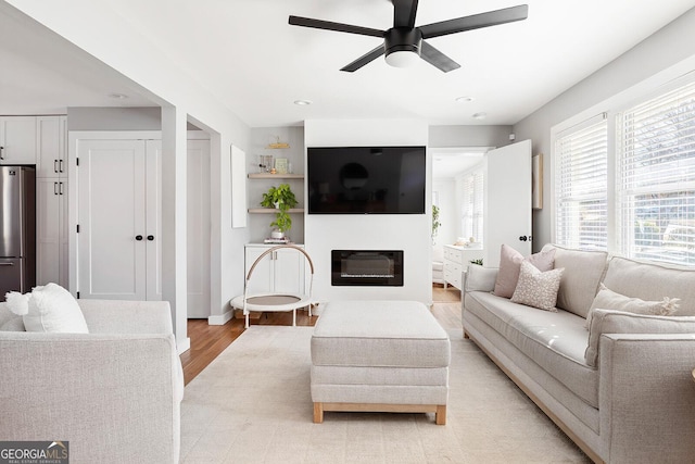 living area featuring light wood-type flooring, a glass covered fireplace, and ceiling fan