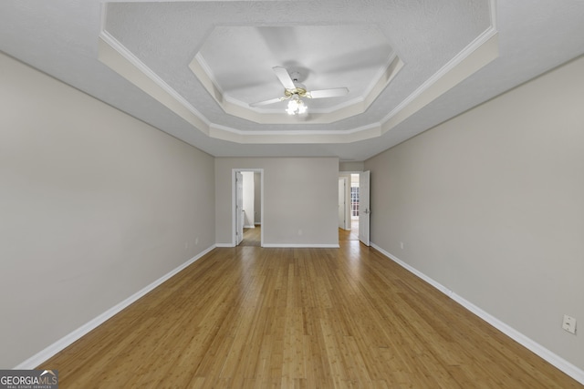 unfurnished room with baseboards, a ceiling fan, light wood-style flooring, a tray ceiling, and crown molding