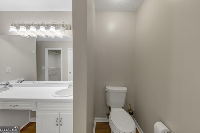 half bathroom with toilet, baseboards, a textured ceiling, and vanity